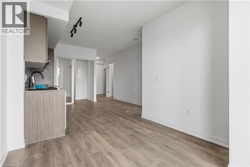 The property features durable wood-look flooring throughout, a modern kitchen with light wood-grain cabinetry, and a sleek black faucet - 4878 Powers Common Unit# 224, Burlington, ON - Indoor Photo Showing Other Room
