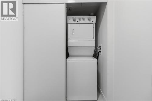 Laundry area featuring a stacked washer and dryer unit, conveniently located behind a sliding door - 4878 Powers Common Unit# 224, Burlington, ON - Indoor Photo Showing Laundry Room