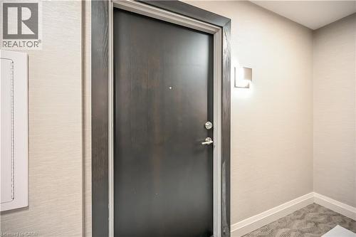 Entryway featuring a dark wood door with chrome hardware, textured wallpaper, and a contemporary wall sconce - 385 Winston Road Unit# 1607, Grimsby, ON - Indoor Photo Showing Other Room