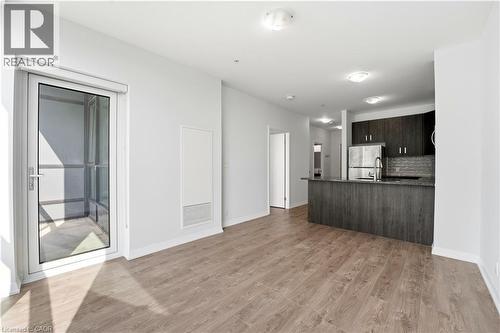 The open concept living area features light-colored wood-style flooring, a glass-paned door leading to a balcony, and a kitchen with dark cabinetry, stainless steel appliances, and a breakfast bar - 104 Garment Street Unit# 1206, Kitchener, ON - Indoor Photo Showing Kitchen