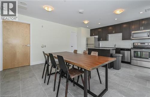 Open-concept kitchen and dining area featuring dark cabinetry, stainless steel appliances, and a tiled backsplash, all complemented by light-colored walls and tiled flooring - 104 Garment Street Unit# 1206, Kitchener, ON - Indoor Photo Showing Kitchen With Stainless Steel Kitchen