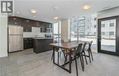 Open concept kitchen and dining area featuring dark wood cabinetry, stainless steel appliances, and large windows with an exterior door - 104 Garment Street Unit# 1206, Kitchener, ON - Indoor