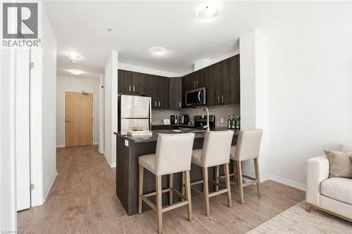 The modern kitchen features dark cabinetry, stainless steel appliances, and a breakfast bar with seating, complemented by light-toned flooring throughout - 104 Garment Street Unit# 1206, Kitchener, ON - Indoor Photo Showing Kitchen