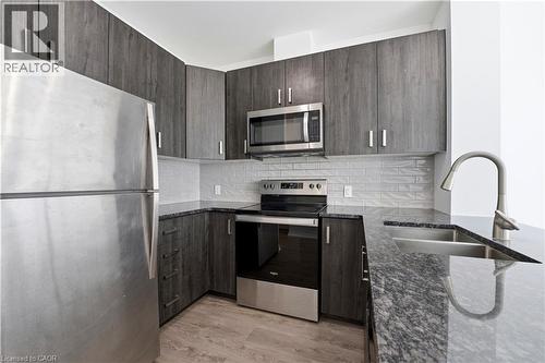 The kitchen features stainless steel appliances, grey wood cabinetry with silver hardware, a dual basin sink with a high arc faucet, and dark granite countertops - 104 Garment Street Unit# 1206, Kitchener, ON - Indoor Photo Showing Kitchen With Stainless Steel Kitchen With Double Sink With Upgraded Kitchen