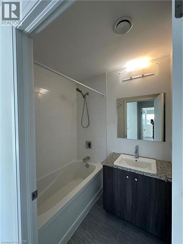 The bathroom features a bathtub with a tiled surround, a vanity with a granite countertop, and a mirror - 108 Garment Street S Unit# 708, Kitchener, ON - Indoor Photo Showing Bathroom