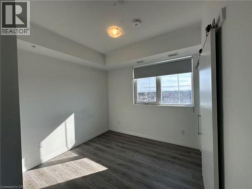 This property features a room with wood-style flooring, a window with a roll-down blind, and a sliding barn door - 108 Garment Street S Unit# 708, Kitchener, ON - Indoor Photo Showing Other Room