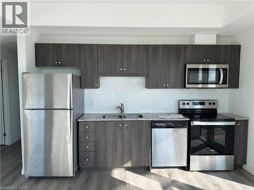The kitchen features wood-look cabinetry, stainless steel appliances, a white subway tile backsplash, and a double basin sink - 108 Garment Street S Unit# 708, Kitchener, ON - Indoor Photo Showing Kitchen With Double Sink