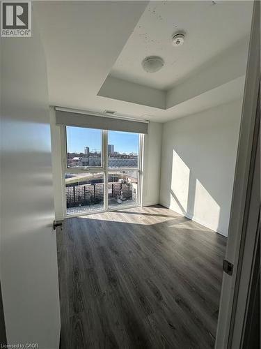 This room features a window with a roller shade, wood-look flooring, and a ceiling light fixture - 108 Garment Street S Unit# 708, Kitchener, ON - Indoor Photo Showing Other Room