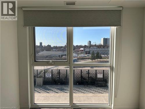 The property features a window with a roller shade, offering views of the surrounding urban landscape and a patterned privacy screen on the patio - 108 Garment Street S Unit# 708, Kitchener, ON - Indoor Photo Showing Other Room