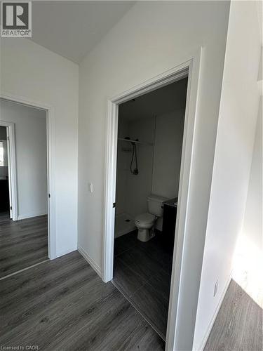 The property features light-colored walls and dark wood-look flooring throughout, with a bathroom visible through a doorway showcasing dark tiled flooring, a toilet, and a shower area - 108 Garment Street S Unit# 708, Kitchener, ON - Indoor Photo Showing Other Room