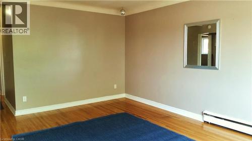 This living space features hardwood flooring, neutral-toned walls with white trim, and a wall-mounted mirror - 981 Mohawk Road E, Hamilton, ON - Indoor Photo Showing Other Room