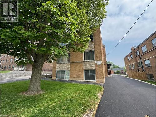 The property features a brick exterior with stone accents, a well-maintained lawn with a mature tree, and a paved driveway - 981 Mohawk Road E, Hamilton, ON - Outdoor