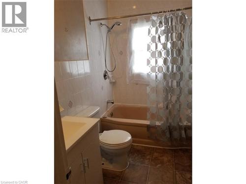 Bathroom featuring tiled walls, a bathtub with an overhead shower, a toilet, and a vanity with a sink - 981 Mohawk Road E, Hamilton, ON - Indoor Photo Showing Bathroom