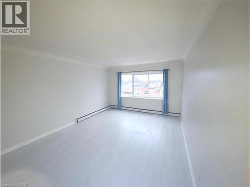 Spacious living area featuring light-colored flooring, white walls, and a large window with blue curtains providing natural light - 981 Mohawk Road E, Hamilton, ON - Indoor Photo Showing Other Room