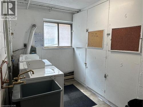 The laundry area features two washing machines, a utility sink with brass fixtures, and a series of built-in storage lockers - 981 Mohawk Road E, Hamilton, ON - Indoor