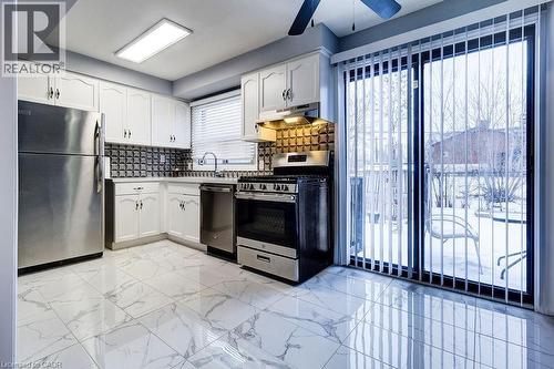 The kitchen features stainless steel appliances, white cabinetry, a patterned backsplash, and large sliding glass doors providing access to the outdoors - 687 Britannia Avenue, Hamilton, ON - Indoor Photo Showing Kitchen With Stainless Steel Kitchen