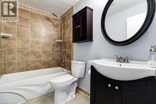 Bathroom featuring a white bathtub, a tiled shower surround, a dark wood vanity with a white basin, and an oval mirror - 687 Britannia Avenue, Hamilton, ON - Indoor Photo Showing Bathroom