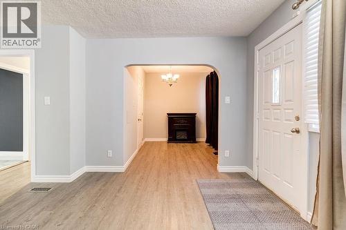 Foyer with light-colored flooring, a white entry door with a window, and an arched doorway leading to an interior space featuring a dark-colored decorative fireplace and a chandelier - 687 Britannia Avenue, Hamilton, ON - Indoor Photo Showing Other Room