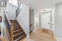 Foyer with light hardwood floors, a white main entry door, and a staircase featuring wooden treads and railings with black spindles - 
