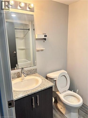The bathroom features a vanity with a granite countertop, a basin sink, and a dark wood-look cabinet with silver handles - 275 Larch Street Unit# 108, Waterloo, ON - Indoor Photo Showing Bathroom