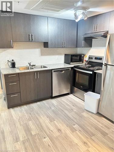 Kitchen featuring wood-look flooring, grey cabinetry with silver hardware, granite countertops, and a subway tile backsplash - 275 Larch Street Unit# 108, Waterloo, ON - Indoor Photo Showing Kitchen With Double Sink