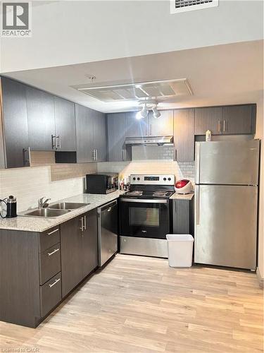 The kitchen features dark wood cabinetry, granite-style countertops, and light-toned flooring - 275 Larch Street Unit# 108, Waterloo, ON - Indoor Photo Showing Kitchen With Double Sink
