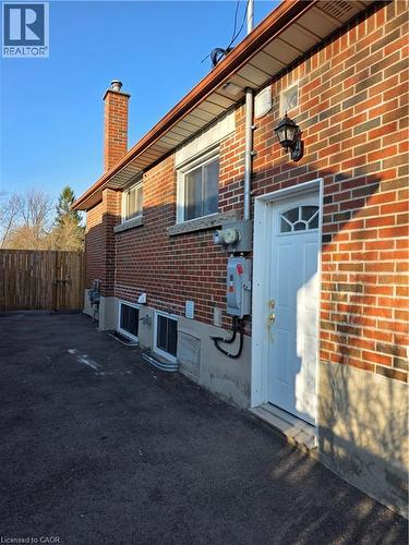 The property features a brick exterior with a chimney, a white exterior door, and a paved surface - 62 Richwill Road Unit# Lower, Hamilton, ON - Outdoor With Exterior