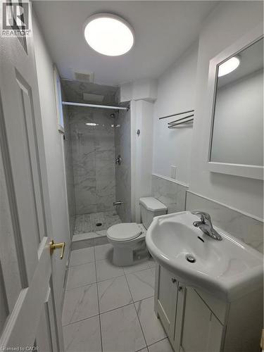 This bathroom features a shower with marble-patterned tile, a vanity with a white sink, and light-colored tile flooring - 62 Richwill Road Unit# Lower, Hamilton, ON - Indoor Photo Showing Bathroom