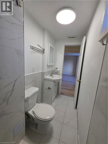 The bathroom features a toilet, a shower area with white marble-patterned tiles, and a vanity with a white basin sink - 62 Richwill Road Unit# Lower, Hamilton, ON - Indoor Photo Showing Bathroom