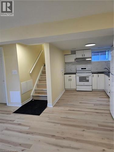 The property features light-toned flooring, a staircase with a handrail, and a kitchen area with white cabinetry, a white stove, and a tiled backsplash - 62 Richwill Road Unit# Lower, Hamilton, ON - Indoor