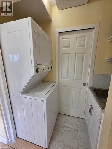 Laundry area featuring a stacked washer and dryer, tiled flooring, and a utility sink with white cabinetry - 62 Richwill Road Unit# Upper, Hamilton, ON - Indoor Photo Showing Laundry Room