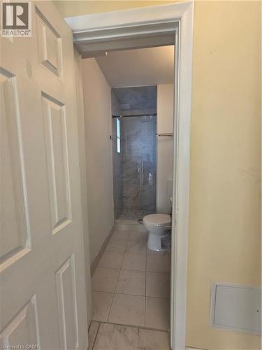 The bathroom features light-colored tile flooring, a toilet, and a walk-in shower with a glass door and tiled walls - 62 Richwill Road Unit# Upper, Hamilton, ON - Indoor Photo Showing Bathroom