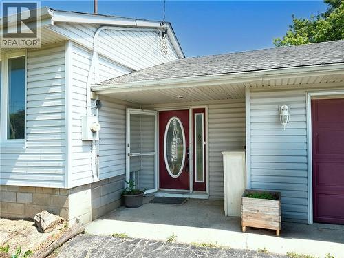 Exterior featuring light-colored siding, a red entry door with an oval glass insert, and a matching red garage door - 9183 Silver Street, Caistor Centre, ON - Outdoor With Exterior