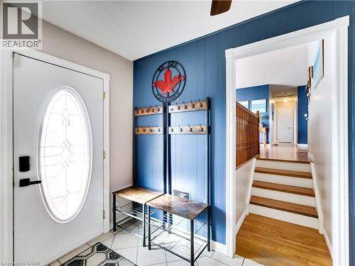 Entryway featuring a decorative glass insert door, tiled flooring, vertical plank accent wall, and a staircase with wood-finish treads and a wooden railing - 9183 Silver Street, Caistor Centre, ON - Indoor Photo Showing Other Room