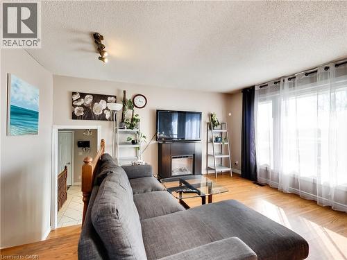 Living area featuring wood-finish flooring, a wall-mounted fireplace with a dark surround, and large windows with sheer and blackout curtains - 9183 Silver Street, Caistor Centre, ON - Indoor Photo Showing Living Room
