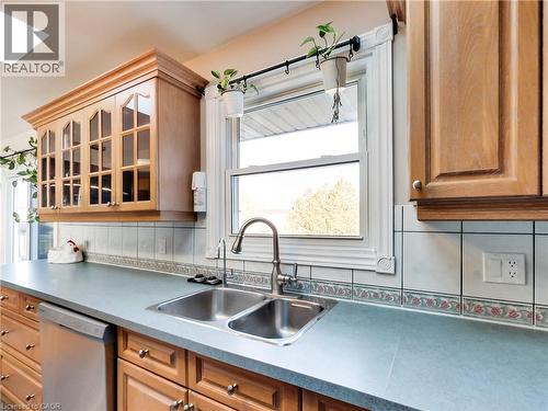 Kitchen featuring light wood cabinetry with glass-front uppers, a dual-basin stainless steel sink with a gooseneck faucet, light blue countertops, and white square tile backsplash with a decorative bo - 9183 Silver Street, Caistor Centre, ON - Indoor Photo Showing Kitchen With Double Sink