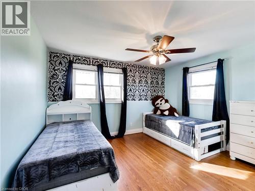 Room featuring wood-finish flooring, light blue and patterned wallpaper walls, a ceiling fan with integrated lighting, and two windows providing natural illumination - 9183 Silver Street, Caistor Centre, ON - Indoor Photo Showing Bedroom