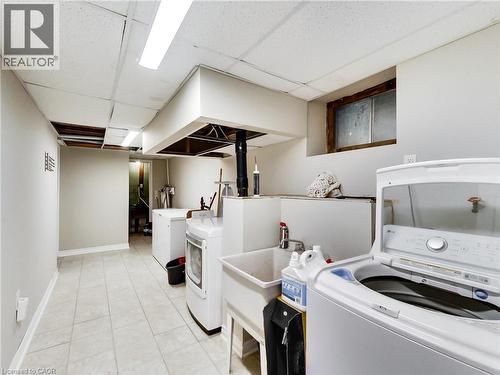 Spacious utility room featuring light-toned tile flooring, drop ceiling with fluorescent lighting, and a utility sink - 9183 Silver Street, Caistor Centre, ON - Indoor Photo Showing Laundry Room