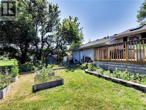 Rear exterior featuring a wood deck with wood railings, siding, and a sloped backyard with raised garden beds and mature trees - 9183 Silver Street, Caistor Centre, ON - Outdoor With Deck Patio Veranda