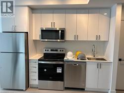 The kitchen features a full suite of stainless steel appliances, including a refrigerator, range, microwave, and dishwasher - 