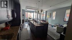 Open-concept living area featuring a kitchen with granite countertops and dark cabinetry, and hardwood floors extending into the dining area - 