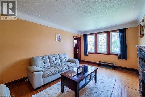 Living area featuring wood-finish flooring, a three-panel window array, and a brick fireplace - 66 Cline Avenue Unit# Main Floor, Hamilton, ON - Indoor Photo Showing Living Room