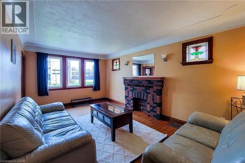 Living area featuring a brick fireplace with wood mantel, hardwood flooring, and multiple windows - 66 Cline Avenue Unit# Main Floor, Hamilton, ON - Indoor Photo Showing Living Room