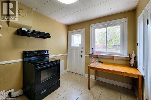Kitchen featuring a black electric range with an overhead exhaust fan, a white paneled door, and a sliding window - 66 Cline Avenue Unit# Main Floor, Hamilton, ON - Indoor