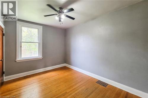 Hardwood flooring throughout featuring white baseboards, a ceiling fan with integrated lighting, a double-hung window with white trim, and a wood-paneled door - 66 Cline Avenue Unit# Main Floor, Hamilton, ON - Indoor Photo Showing Other Room