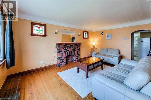 Living area featuring wood-finish flooring, a brick-detailed fireplace with a wooden mantel, and a stained-glass window accent - 66 Cline Avenue Unit# Main Floor, Hamilton, ON - Indoor Photo Showing Living Room With Fireplace