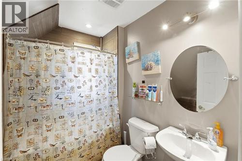 The bathroom features a shower area with tiled walls, a toilet, a wall-mounted sink with a chrome faucet, and a circular mirror with a track lighting fixture above - 99 Robins Avenue, Hamilton, ON - Indoor Photo Showing Bathroom