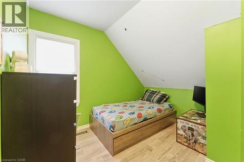 This room features a window providing natural light, bright green walls, and light-colored flooring - 99 Robins Avenue, Hamilton, ON - Indoor Photo Showing Bedroom