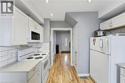 The kitchen features white cabinetry, a white stove with an overhead microwave, and light-colored countertops - 99 Robins Avenue, Hamilton, ON - Indoor Photo Showing Kitchen