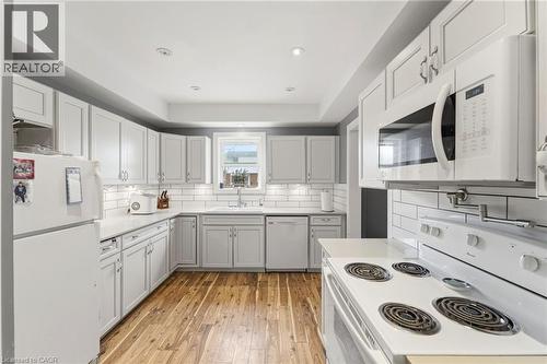 The kitchen features white cabinetry, white appliances, a white subway tile backsplash, and wood flooring - 99 Robins Avenue, Hamilton, ON - Indoor Photo Showing Kitchen